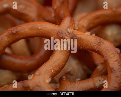 Un gros plan macro de bretzels salés croustillants au four avec des cristaux de sel grossier éparpillés sur leur surface dorée Banque D'Images