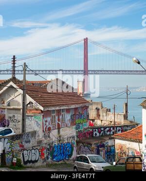 LISBONNE, PORTUGAL - nov 09, 2025 : vieux bâtiments couverts de graffitis vibrants se dressent près du front de mer à Almada, Portugal, avec le 25 avril Bridg Banque D'Images