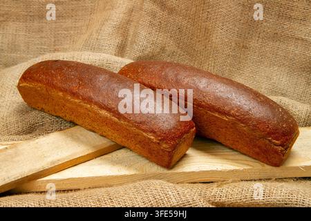 Deux pains de seigle sur une toile de jute. Produits de boulangerie sur des planches. Banque D'Images