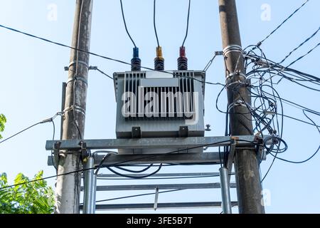 Transformateur électrique monté sur des poteaux en béton avec un câblage emmêlé contre un ciel bleu Banque D'Images
