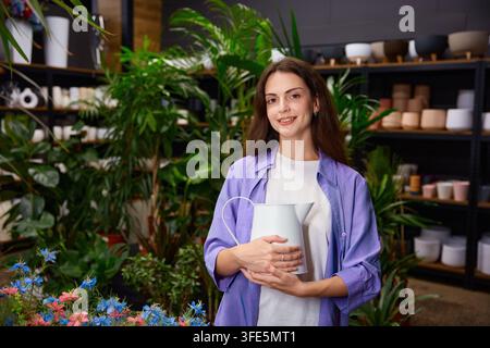 Femme tenant un vase en céramique dans un atelier boutique avec des étagères en arrière-plan Banque D'Images