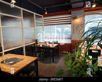 Intérieur moderne d'un restaurant coréen en Corée avec des tables en bois, des chaises noires, des plantes et des cloisons en verre dépoli. Banque D'Images
