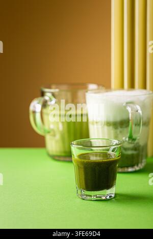 Boissons au latte matcha et au thé vert présentées dans des verres sur une surface verte vibrante avec un fond brun chaud Banque D'Images