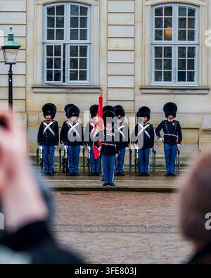 Copenhague, Danemark - décembre 2025 : des membres des Gardes de la Vie royale danoise, coiffés de bonnets en peau d'ours, se tiennent au garde-à-vous devant le palais d'Amalienborg alors que des passants Banque D'Images
