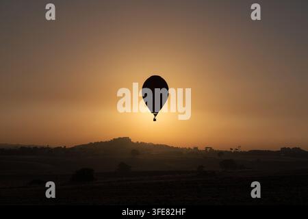Vue d'un ballon à air chaud en silhouette contre le coucher de soleil doré sur le paysage rural de Gravina in Puglia, Pouilles, Italie. Banque D'Images