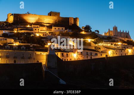 Vue du château de Mertola illuminé surplombant la ville historique aux maisons blanches et à une église sous un ciel crépusculaire clair à Mertola, district de Beja Banque D'Images