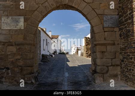 Vue d'une arche en pierre historique menant aux rues pavées étroites du village médiéval de Monsaraz, dans le district d'Évora, au Portugal. Banque D'Images