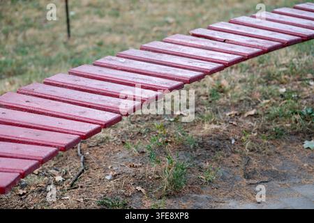 Banc de jardin en bois rouge s'étend en diagonale sur un parc herbeux, avec des planches peintes patinées et un espace ouvert autour de la structure. Convient Banque D'Images