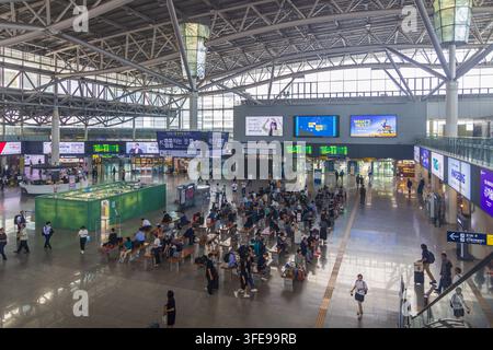 Les passagers se déplacent et attendent dans un grand hall de gare avec des panneaux de départ, des panneaux en langue coréenne, des magasins, des publicités et un toit en acier élevé. Banque D'Images