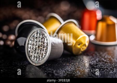 Des capsules de café métalliques usagées et des grains de café torréfiés dispersés reposent sur une surface sombre et texturée, évoquant un rituel matinal, une dose unique pratique Banque D'Images