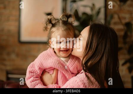 Mère aimante embrassant la joue de sa mignonne petite fille portant des pulls roses assortis Banque D'Images