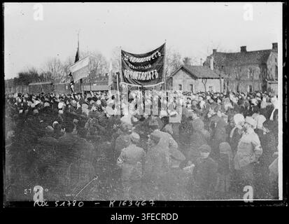 Une grande foule de personnes rassemblée en plein air en Roumanie pendant la Première Guerre mondiale, beaucoup portant des chapeaux et des manteaux, debout devant un train et des bâtiments, avec des bannières brandies, l'une portant des inscriptions visibles, alors qu'ils semblent observer ou participer à une manifestation, par Agence Rol en 1918. Banque D'Images