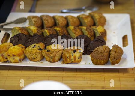 Un assortiment de muffins fraîchement cuits et de pains rapides tranchés servis sur un plateau blanc pour un petit-déjeuner buffet. Banque D'Images