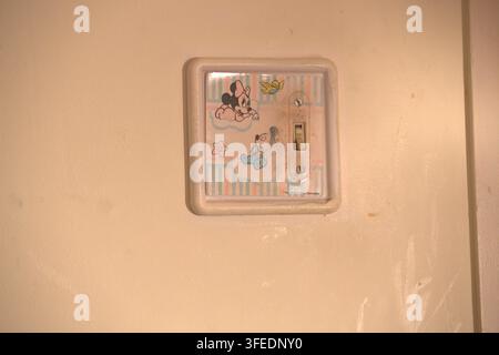 Une plaque d'interrupteur vintage avec des illustrations de personnages de dessins animés pastel montée sur un mur intérieur crème dans une chambre d'enfant à la maison. Banque D'Images