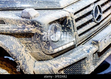 Gros plan du phare avant, de la calandre et du pare-chocs d'un SUV de luxe noir entièrement recouvert de grosses éclaboussures de boue après une aventure tout-terrain. Banque D'Images