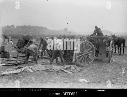 Une photographie de presse de 1916 par Agence Rol, présentant plusieurs hommes en uniforme chargeant ou déchargeant des caisses en bois d'un grand chariot à deux roues tiré par un cheval, au milieu d'une scène de la Première Guerre mondiale avec des projectiles. Banque D'Images