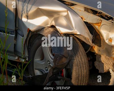 Grossissement d'une voiture argentée lourdement endommagée montrant un pare-chocs fortement cabossé, un passage de roue écrasé et des panneaux de carrosserie rouillés Banque D'Images
