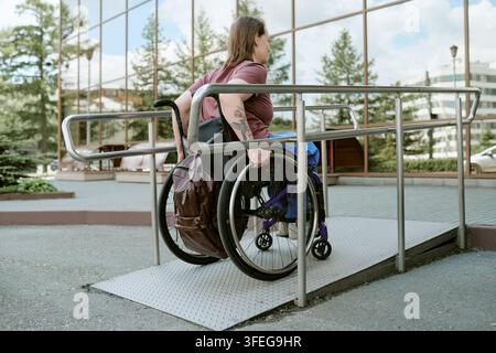 Femme en fauteuil roulant avec handicap utilisant une rampe extérieure accessible Banque D'Images