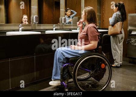 Femme en fauteuil roulant appliquant du baume à lèvres dans les toilettes Banque D'Images