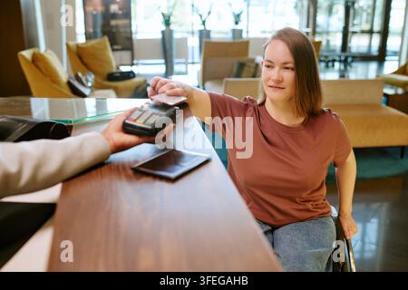Femme handicapée payant avec une carte de crédit à la réception de l'hôtel Banque D'Images