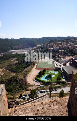 Une vue en contre-plongée mettant en valeur un paysage urbain pittoresque avec un terrain de football, des piscines et une végétation luxuriante, le tout sous un ciel bleu clair. Banque D'Images