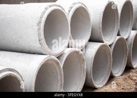 Tubes de drainage en béton empilés en formation pyramidale sur un chantier de construction en terre, les joints arrondis visibles le long des rangées, la lumière du matin projette des ombres douces à travers Banque D'Images