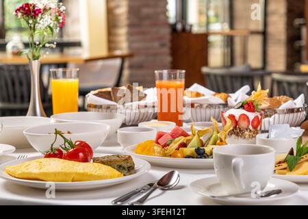 Table de brunch luxueuse avec omelette, tomates, pâtisseries, fruits et thé Banque D'Images