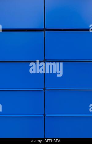 Grossissement de panneaux muraux en métal bleu vif disposés selon une grille régulière, créant une texture industrielle géométrique audacieuse et un fond abstrait Banque D'Images