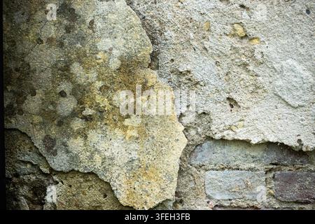 Le plâtre jaune qui s'écaille révèle un ciment gris rugueux en dessous, créant une texture de mur vieillie et abîmée avec des fissures, des taches et de la dégradation Banque D'Images