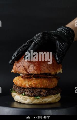 Main gantée ajoute la touche finale à un burger artisanal Banque D'Images