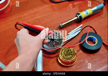 Photographie amateur en gros plan horizontale mettant en vedette une variété d'outils de soudure et d'électronique disposés sur une table en bois, tandis qu'une main de femme tient Banque D'Images
