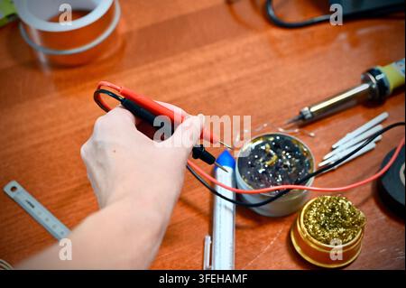 Photographie amateur en gros plan horizontale mettant en vedette une variété d'outils de soudure et d'électronique disposés sur une table en bois, tandis qu'une main de femme tient Banque D'Images