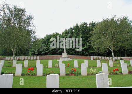 La croix blanche en pierre du Sacrifice se dressant parmi des rangées de pierres tombales derrière un mur de soutènement en brique bas dans un cimetière militaire du Commonwealth en Belgique. Banque D'Images