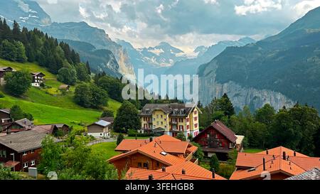 Village alpin suisse surplombant une vallée montagneuse spectaculaire. Village alpin suisse avec des chalets en bois et des toits rouges surplombant une vallée montagneuse luxuriante Banque D'Images