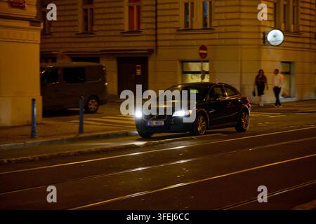 Une berline Volvo roule de nuit le long du quai Masaryk à côté des voies de tramway dans le centre de Prague. Banque D'Images