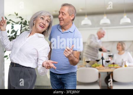 Couple mûr exécutant une danse en couple dos à dos, exécutant une danse amateur boogie, s'amusant, flirtant dans le salon. Événement familial Banque D'Images