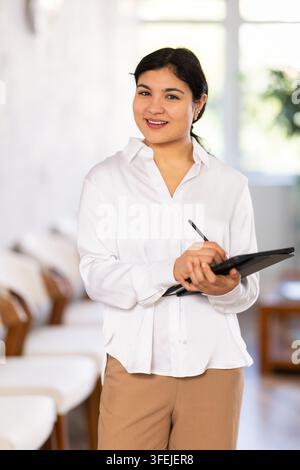 Jeune employée avec tablette debout dans la zone de réception. Gestionnaire d'hôtellerie, réceptionniste ou spécialiste du contrôle d'accès, hôtesse de bureau. Banque D'Images