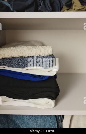 Vue verticale d'une pile soigneusement rangée de pulls tricotés chauds dans une armoire, adaptée aux concepts d'organisation des vêtements d'automne et d'hiver. Banque D'Images