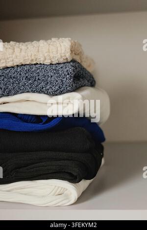 Photographie verticale d'une pile soigneusement pliée de pulls chauds dans une garde-robe minimaliste, représentant le rangement organisé des vêtements d'automne et d'hiver. Banque D'Images