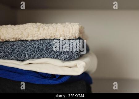 Pile soigneusement pliée de pulls chauds dans une armoire propre, mettant en évidence le rangement organisé des vêtements et la préparation pour la saison automnale et hivernale Banque D'Images