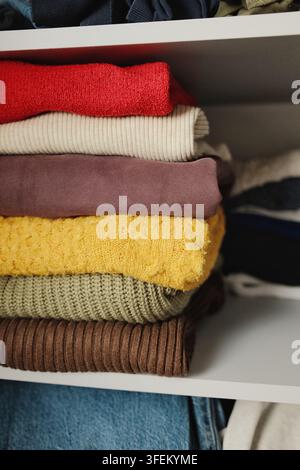 Vue rapprochée de pulls tricotés colorés pliés disposés sur une étagère de placard, illustrant l'organisation et le rangement des vêtements d'automne et d'hiver Banque D'Images