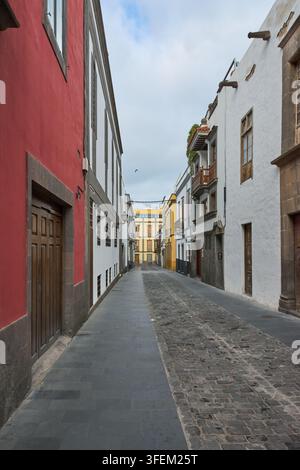 Une rue historique étroite à Vegueta présente des bâtiments coloniaux traditionnels colorés, un pavage en pierre et des portes en bois classiques sous un ciel nuageux Banque D'Images