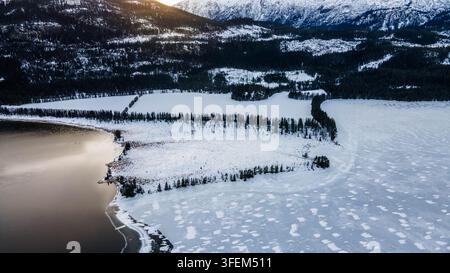 Vue aérienne d'un lac de montagne partiellement gelé entouré de forêts et de montagnes enneigées en Norvège Banque D'Images