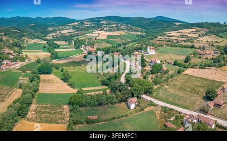 Paysage de la campagne serbe avec un village rural niché parmi des collines verdoyantes, des terres cultivées et des routes sinueuses Banque D'Images