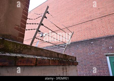 Mur de briques avec barrière de sécurité en fil de fer barbelé, porte métallique verte, caméra de surveillance montée Banque D'Images