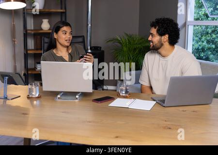 Collaborateurs afro-américains discutant des idées au bureau avec deux ordinateurs portables et un smartphone Banque D'Images