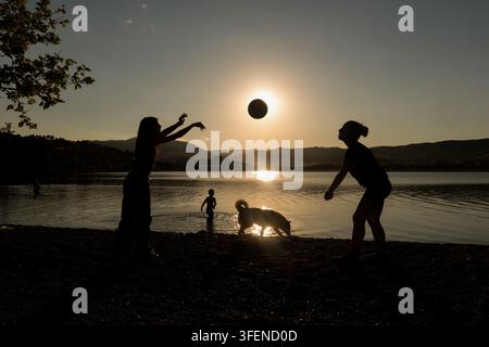 Silhouettes de deux enfants jouant avec un ballon au coucher du soleil sur les rives du lac Lisi à Tbilissi, en Géorgie, avec la lumière du soleil se reflétant sur l'eau Banque D'Images