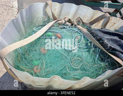 Un filet de pêche en maille verte fin est soigneusement rangé avec des flotteurs orange dans un grand sac souple blanc. Le sac repose sur une surface plane près de la pêche Banque D'Images