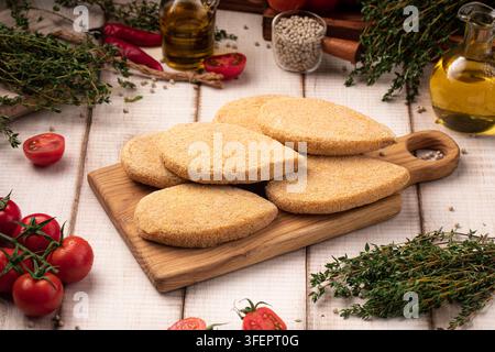 Steaks de poulet panés crus sur planche en bois Banque D'Images