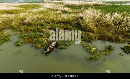 Vue aérienne d'un petit bateau en bois avec une personne naviguant à travers les eaux de la rivière entourées d'herbe blanche kash phool et d'hyacinthe d'eau à Dhaka, Dh Banque D'Images